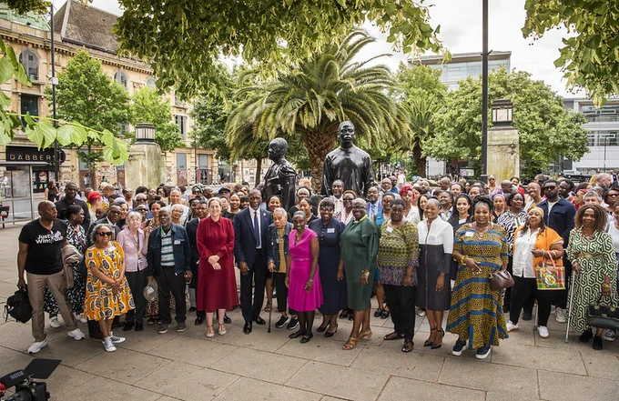 On Wednesday 26 July, 2025, hundreds gathered at Hackney Town Hall to Welcome Rev Clive Foster MBE, the newly appointed Windrush Commissioner. This photograh includes the Mayor and Chief Executive of Hackney standing with Cllr Carole Williams, the lead member for Windrush and Rev Clive Foster MBE. The invited guests stand beside and behind them. In the background, is Warm Shores, the Windrush Artwork by Thomas J Price. 