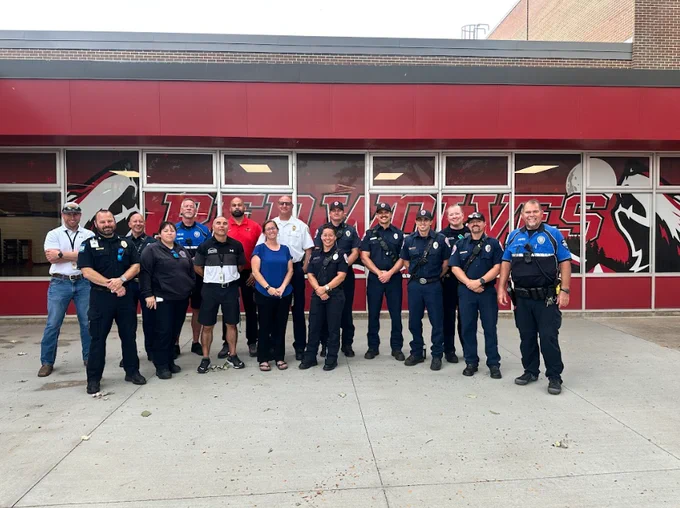 Group of police, fire, and school staff pose together in front of a building with "Red Wolves" on the windows.