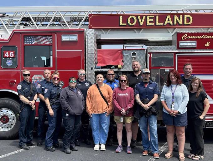 Group of firefighters and school staff stand smiling in front of a red Loveland Fire Rescue Authority truck marked Engine 46.