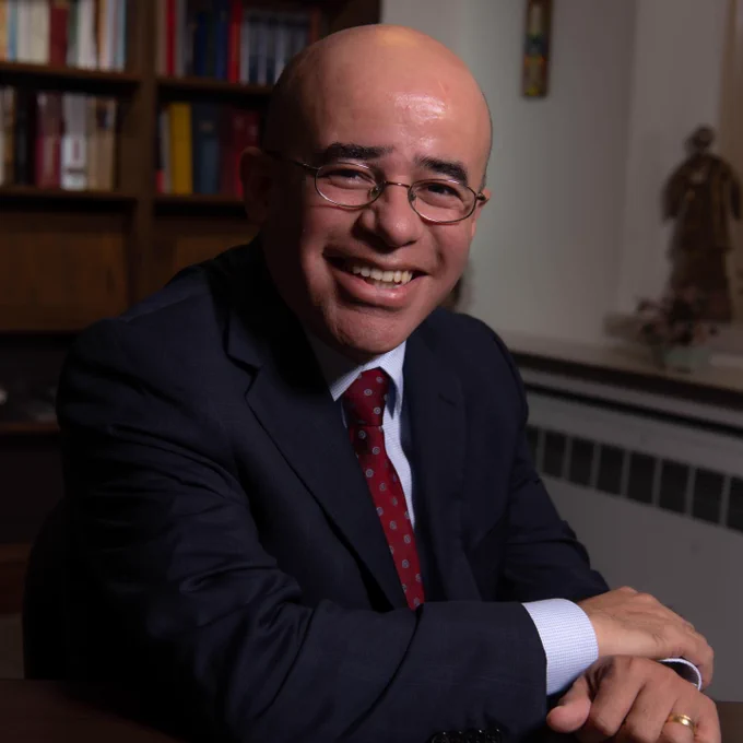 Hosffman Ospino sitting at a desk with a bookshelf in the background