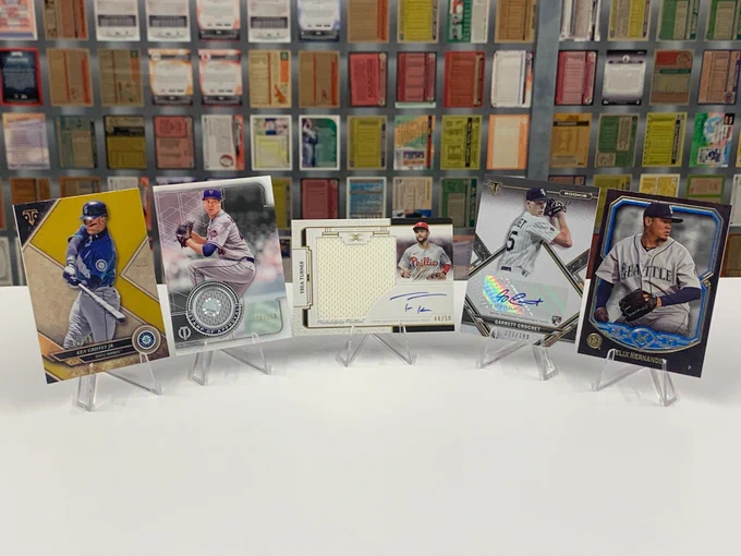 Five baseball cards:
-2017 Topps Triple Threads
Ken Griffey Jr, Seattle Mariners (01/99)
-2019 Topps Tribute Certified Stamp of Approval Relic Card
Jacob deGrom, New York Mets (120/150)
-2024 Topps Definitive Collection Autographed Relic Card
Trea Turner, Philadelphia Phillies 44/50
-2021 Topps Triple Threads Certified Autograph Issue
Garrett Crochet, Chicago White Sox
(177/199)
-2017 Topps Museum Collection
Felix Hernandez, Seattle Mariners
(150/150)
