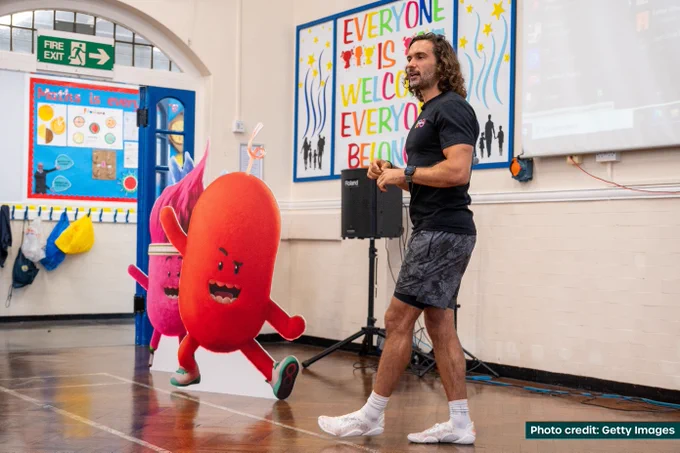 Joe Wicks standing and presenting in front of two colourful, cute mascots from his Activate series