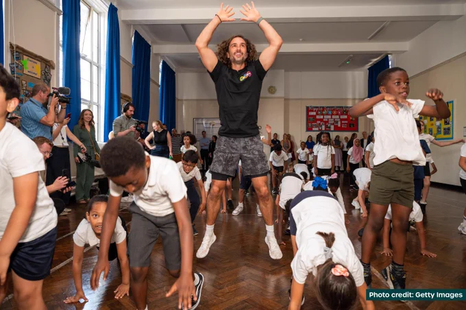 Joe Wicks and schoolchildren in a school assembly hall doing jumping exercises as part of a workout