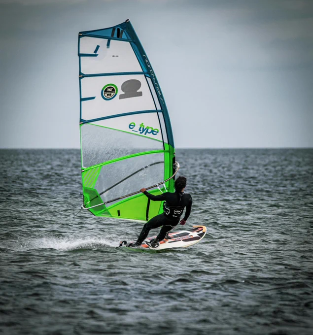 A person on a windsurf board with their back to the camera as they sail towards open waters. 