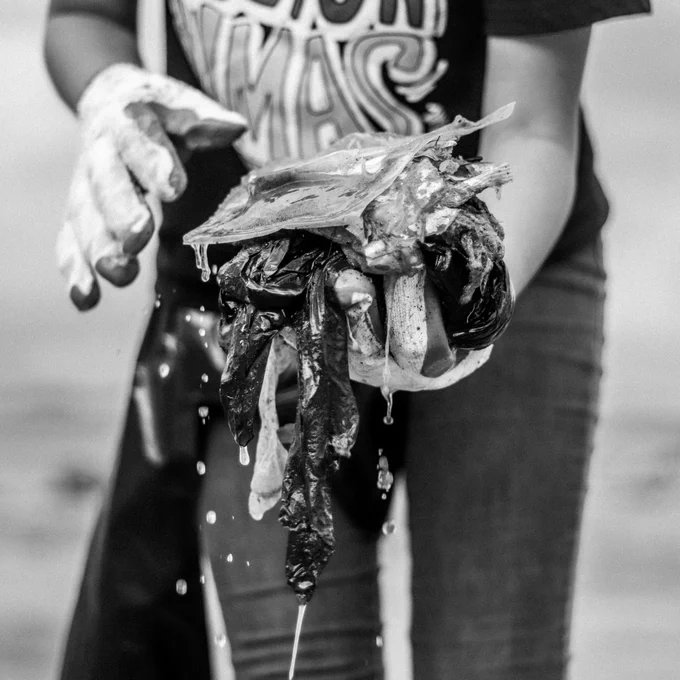 Person beach cleaning with pile of soggy rubbish in gloved hands