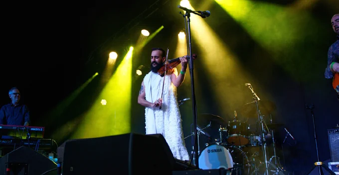 A person playing the violin on stage with a supporting band.
