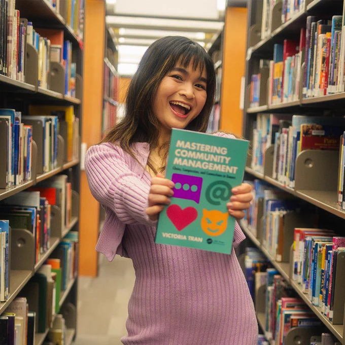 Picture of me in between shelves of books, holding up my book.