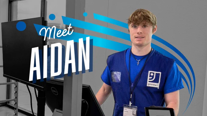 Text "Meet Aidan" with a large blue three lined swoosh going behind text and man standing behind a counter wearing a blue work uniform with Goodwill logo on chest. 