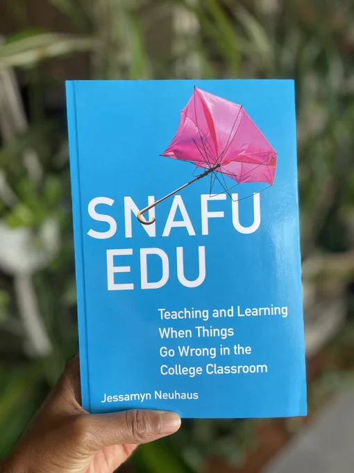 Tolu's hand holding a copy of the book, Snafu Edu, by Jessamyn Neuhaus.
