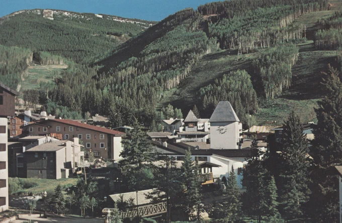View of Vail, Colorado with a variety of buildings in the foreground and densely forested mountain slopes in the background.