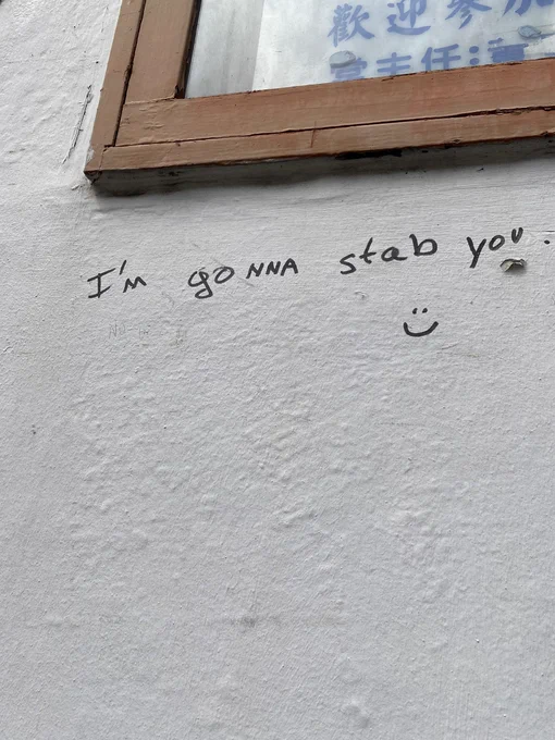 A white wall with the a message written in sharpie “I’m gonna stab you. :)”