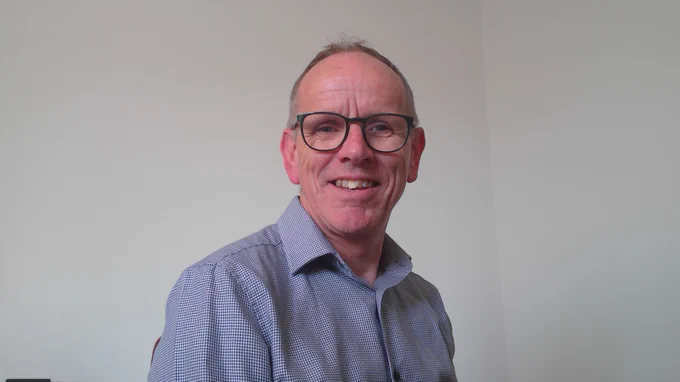Portrait photograph of Alun Owen from the shoulders up, smiling against a white background. 