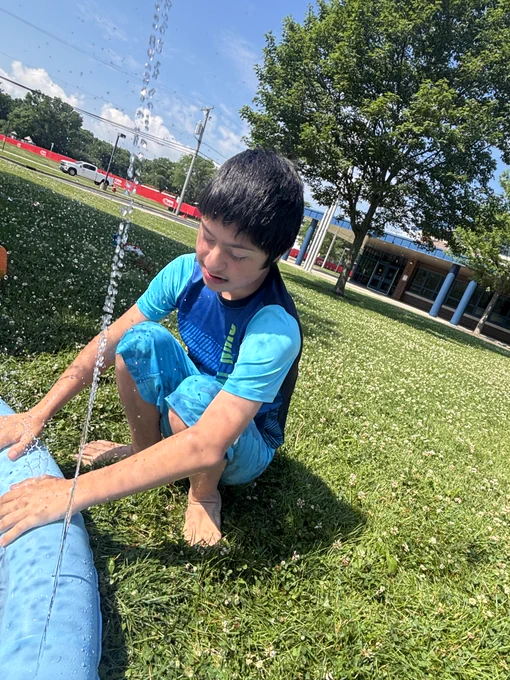 students enjoying water play outdoors with a slip and slide and splash pad
