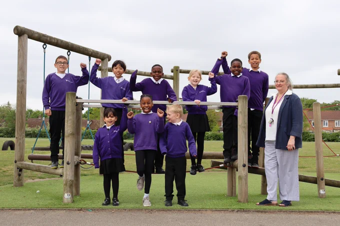 Primary school children and Principal standing on the playground equipment, smiling