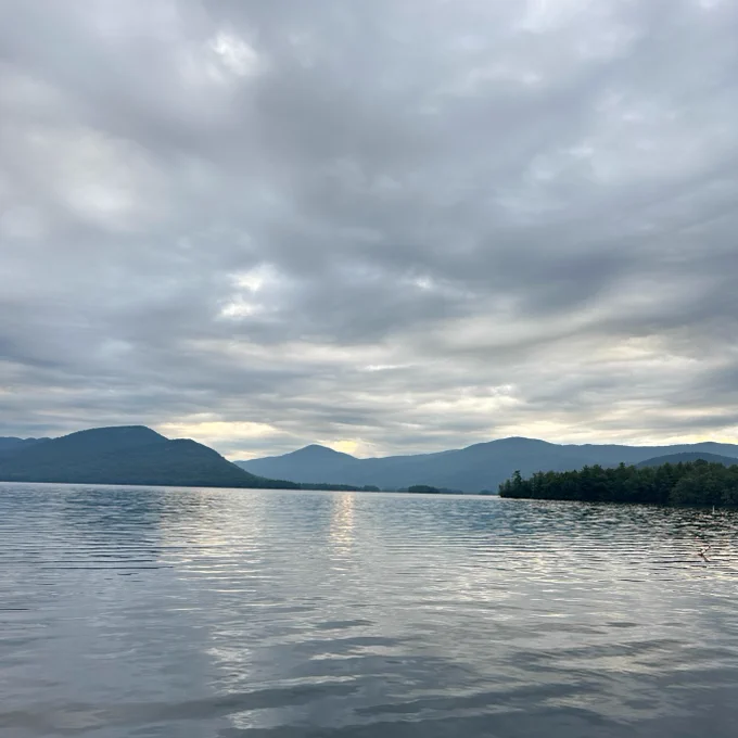 Overcast sky over Lake George with multiple hills in the background.