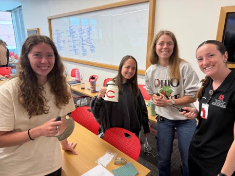 Sam, Greer, Miley, and Emily, second year OT students, learning about adaptive eating utensils and holding some of the adaptive eating utensils.