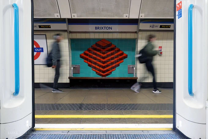 Looking out of the open doors of a 2009 Stock standing at the platform at Brixton, the 'ton of bricks' tiled motif behind a platform bench is perfectly framed, with two blurred passengers either side hurrying past adding to the symmetry.