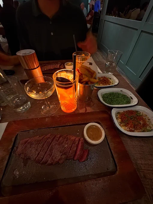 A steak dinner with sides and drinks in a low lit room