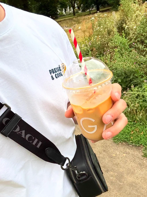 Lewis holding an iced coffee wearing a white t-shirt and a coach cross body bag