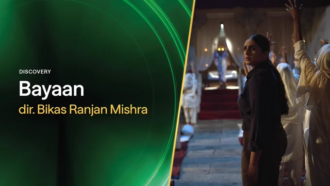 A graphic containing film still from BAYAAN. A woman in dark clothing stands amongst a group of women dressed in white clothing with headscarves. The women in white have their arms raised, facing a figure on a throne-like seat. The graphic reads: "Discovery, Bayaan, dir. Ranjan Mishra"