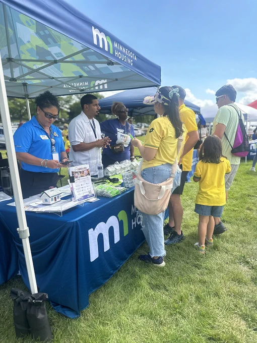Attendees interact with staff at the Minnesota Housing promotional booth on a sunny day.