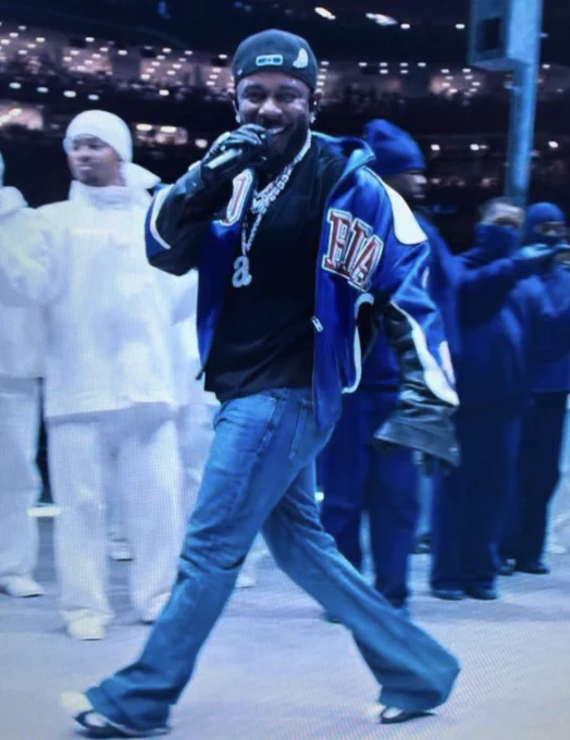 Kendrick Lamar performing his diss track "Not Like Us" on stage during the Super Bowl, wearing a blue jacket.