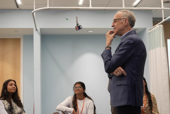 MP Rob Oliphant thoughtfully stands with hand on chin during a group discussion with students in a modern clinical space at Holland Bloorview.