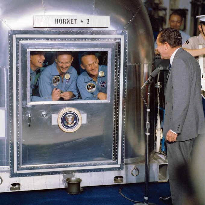 United States President Richard M. Nixon speaks to the Apollo 11 astronauts through a window on the Mobile Quarantine Facility (MQF) aboard the USS Hornet, prime recovery ship for the historic Apollo 11 lunar landing mission. The astronauts in the MQF are (left to right) Neil A. Armstrong, commander; Michael Collins, command module pilot; and Edwin E. Aldrin Jr., lunar module pilot. Apollo 11 splashed down at 11:49 a.m. (CDT), July 24, 1969, about 812 nautical miles southwest of Hawaii and only 12 nautical miles from the USS Hornet. Photo credit: NASA
