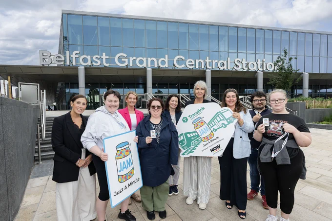 Group shot of Translink & NOW Group staff and service users outside Grand Central Station, holding various Translink & NOW Group/JAM card photo props