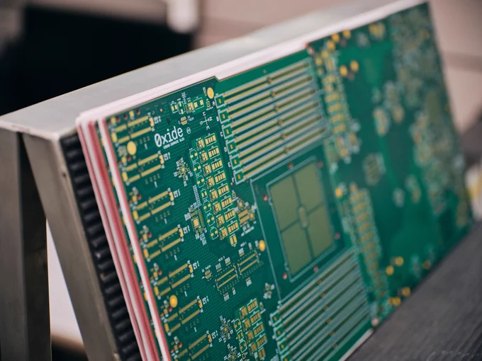 Close-up view of a green Oxide-branded circuit board with gold traces and components during final visual inspection.