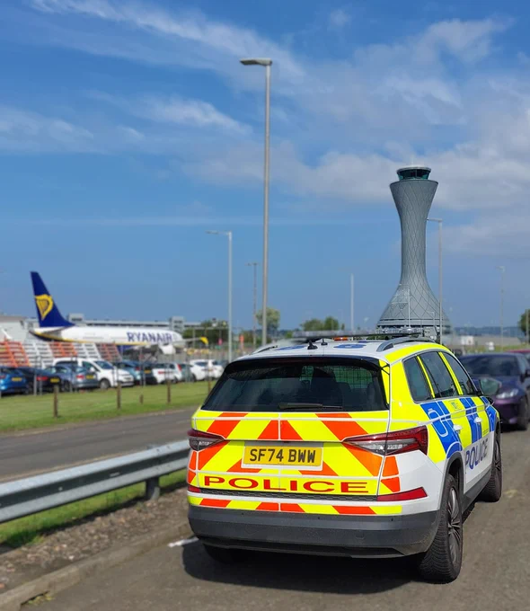 A phot of a marked police vehicle parked at Edinburgh Airport with the control tower and a Ryanair aircraft in the background.