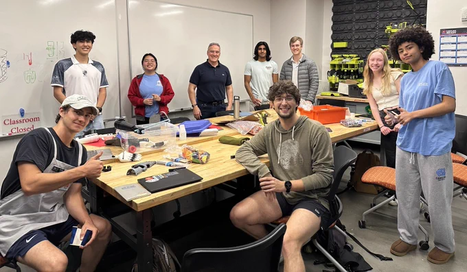 UNC students and Mike Astilla sit at a large work table in the UNC makerspace
