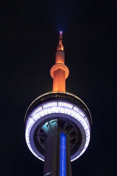 Closeup of the CN Tower at night lit blue, orange and white / Gros plan de la Tour CN illuminée en bleu, orange et blanc la nuit. 