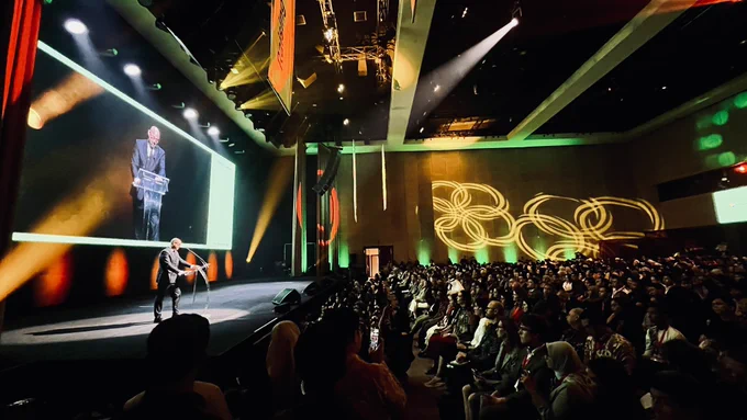 UNFCCC Executive Secretary Simon Stiell speaks on stage at the Indonesia Net Zero Summit 2025 in Jakarta. Wearing a dark suit, he stands at a clear podium in front of a large crowd, with his speech projected on a giant screen behind him. The stage is lit with vibrant green, orange, and red spotlights, and the venue walls are decorated with circular light patterns. The event highlights Indonesia’s leadership potential in Southeast Asia’s clean energy transition and echoes Mr. Stiell’s message that climate ambition and economic development are not opposing goals. (Photo: UN Information Centre Jakarta/Bayu Dwityo Wicaksono)