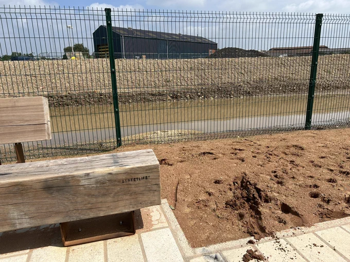 Open ended bench  next to a sandy soil with deep imprints from where my wheelchair sank into