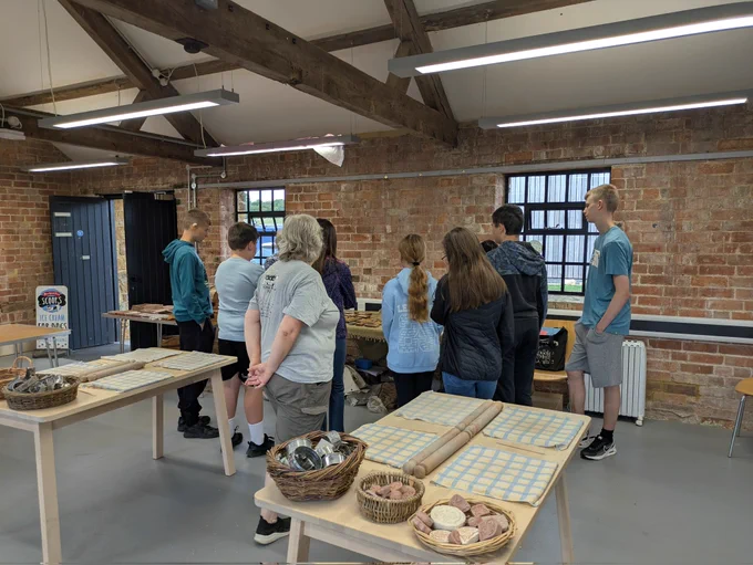 Group of young people stood looking at tables with clay tiles, materials and stations