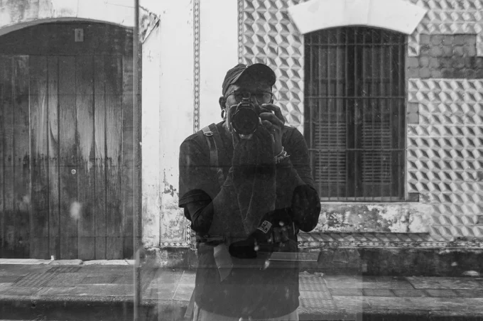 An unexpected self-portrait in relation to what was behind the smoked glass door... In this photograph, I never imagined there would be someone on the other side; I only discovered it when I started editing the photo. On the other side of the door sat the building's security guard, who didn't even realize I was taking pictures. At first, it was supposed to be just my portrait, but I realized that I ended up capturing the other person too!

Work created exclusively for the Reflexos 2025 [OPEN CALL] #BRASILTEZOS Exhibition.