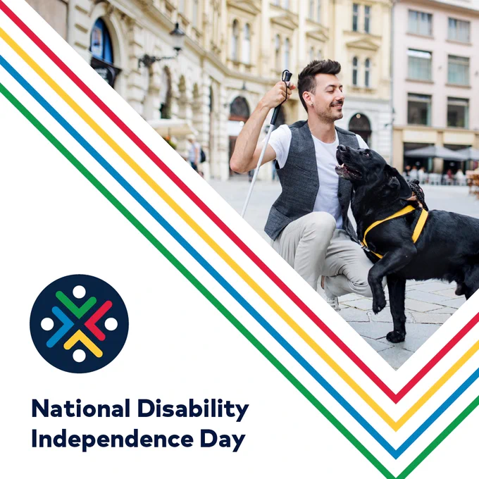 Man with cane smiling and kneeling beside his guide dog with, ‘National Disability Independence Day’