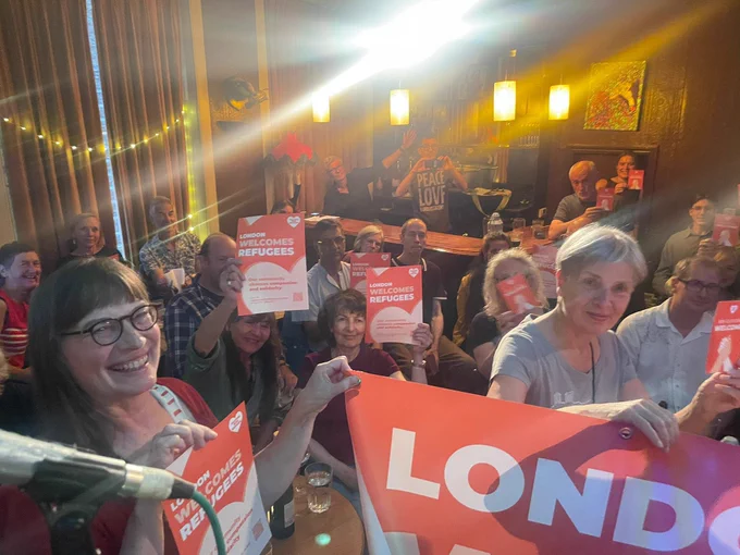 A photo with people carrying posters and cards that read London Welcomes Refugees and We Choose Welcome. Most people in the picture are with smiles.