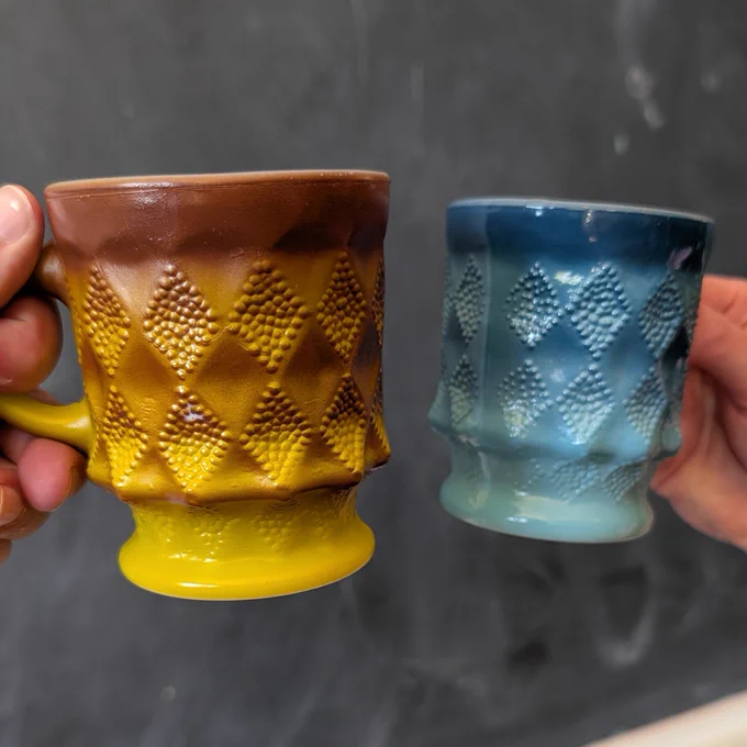 Photograph of two fire king mugs being held in front of a chalkboard at Revolution Hall in Portland, Oregon. 