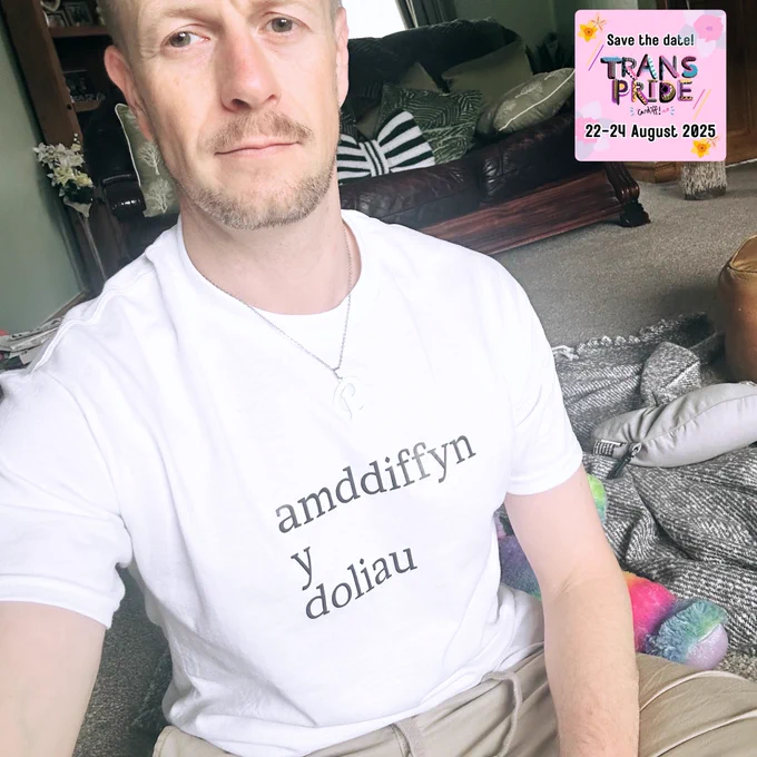 Paul Davies, Welsh actor and presenter, wearing a white t-shirt printed with the Welsh words “amddiffyn y doliau” (Protect the dolls), showing support for the trans community.