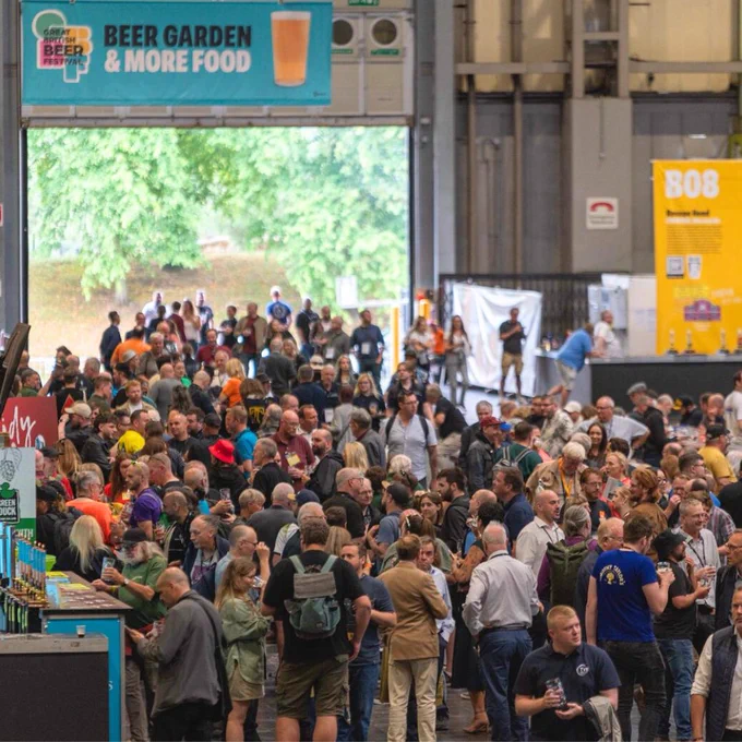 A large crowd of people in a large room with blue and yellow banners. there is a large opening showing trees outside