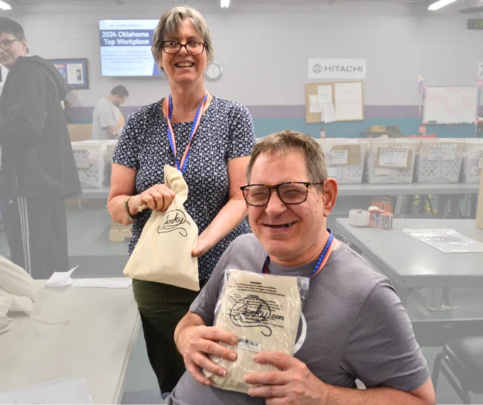 Woman standing over a man's shoulder who is sitting. They are both holding packaged bags with jerky.com logo. 