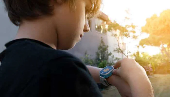 Young boy outdoors checking a blue smartwatch on his wrist, symbolizing the use of GPS watches for kids to ensure safety, location tracking, and digital connectivity.