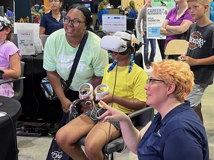 Two visitors experience virtual reality college tours at the Ohio Department of Higher Education booth. 