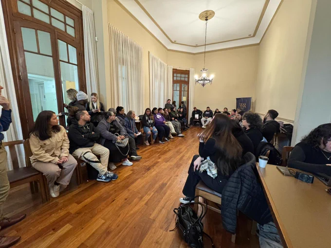 Wide-shot of group photo, participants are sitting along both sides of the room in long rows.

