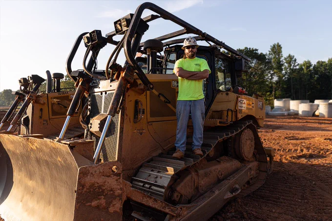 Heavy equipment operator standing on his caterpillar dozer with his arms crossed on a construction site in Charlotte, North Carolina.