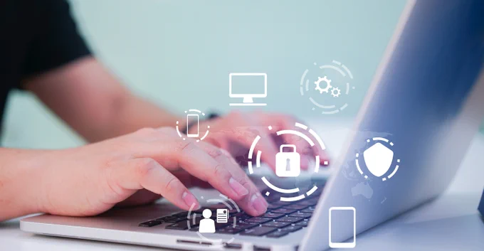 hands typing on a laptop. Graphics in the foreground representing computers, smart phones, and security