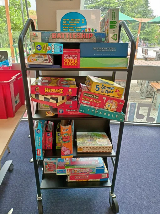 Photograph of board games, including Hedbanz, Scrabble, and Battleship, displayed on a black trolley.