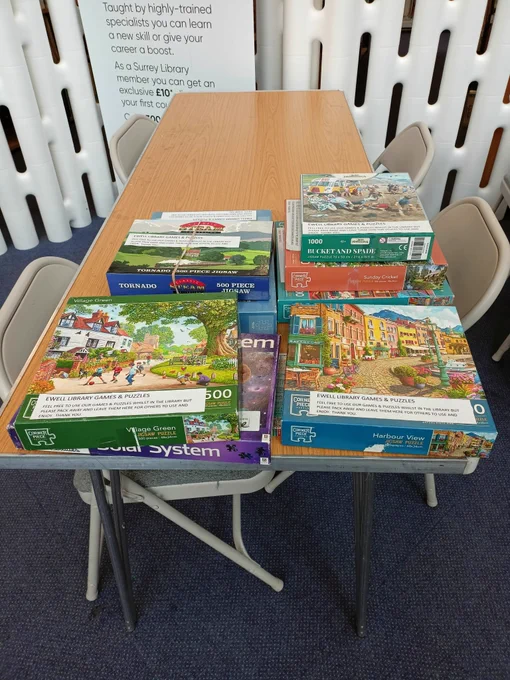 Photograph of a selection of jigsaw puzzles displayed on a long wooden table.